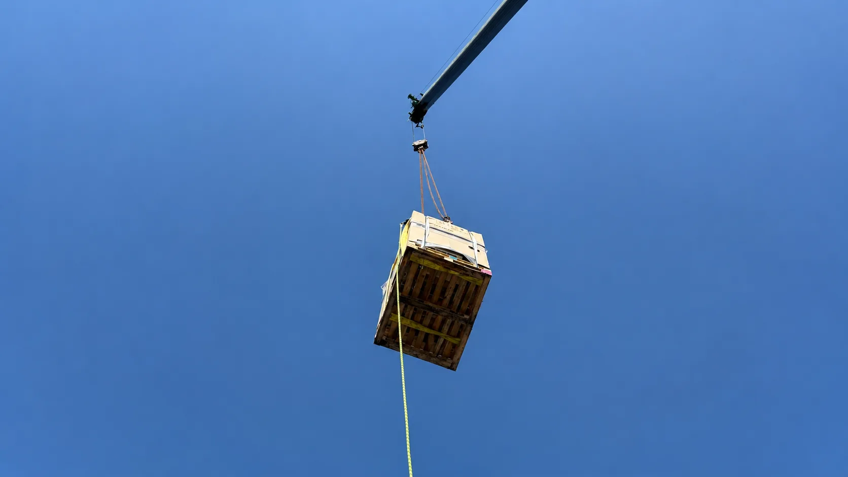 Crane lifting a ventilation unit against a clear blue sky