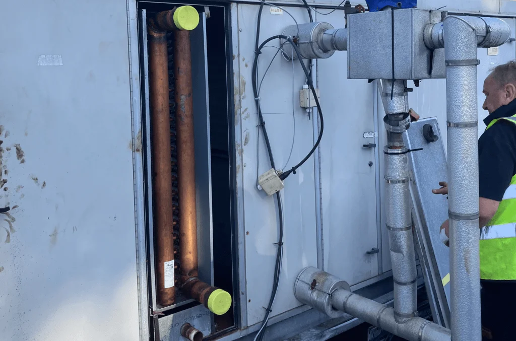 A BVS Worker Performing Maintenance on an open AHU With The Copper Coil Visible