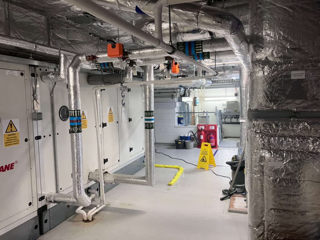 A brightly lit mechanical room with insulated pipes and machinery.